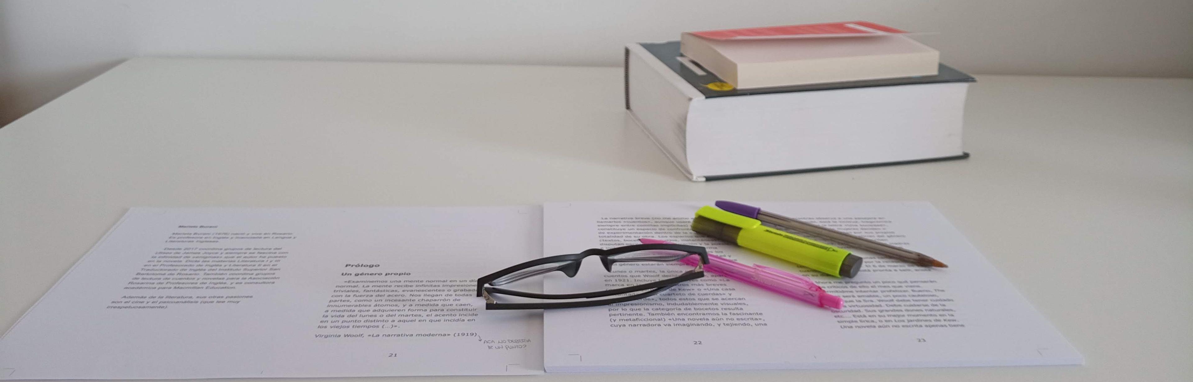 Sobre escritorio blanco se pueden ver varias hojas A4 impresas que aparentan ser la maqueta de un libro. Sobre estas hojas podemos ver unas gafas azules cerradas, un bolígrafo de color rosa, un fibrón resaltador de color amarillo y otro boligrafo abierto de color violeta con la tapa engachada del lado contrario de donde se escribe. En el fondo vemos los lomos delanteros de dos libros. Uno de mayor tamaño y hojas, otro más pequeño con tapa roja encima.